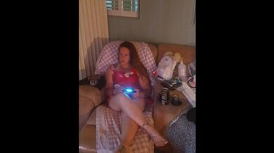 Bella ragazza in mini camicia da notte che gioca ai videogiochi, mentre la coinquilina cerca di filmare il suo vestito